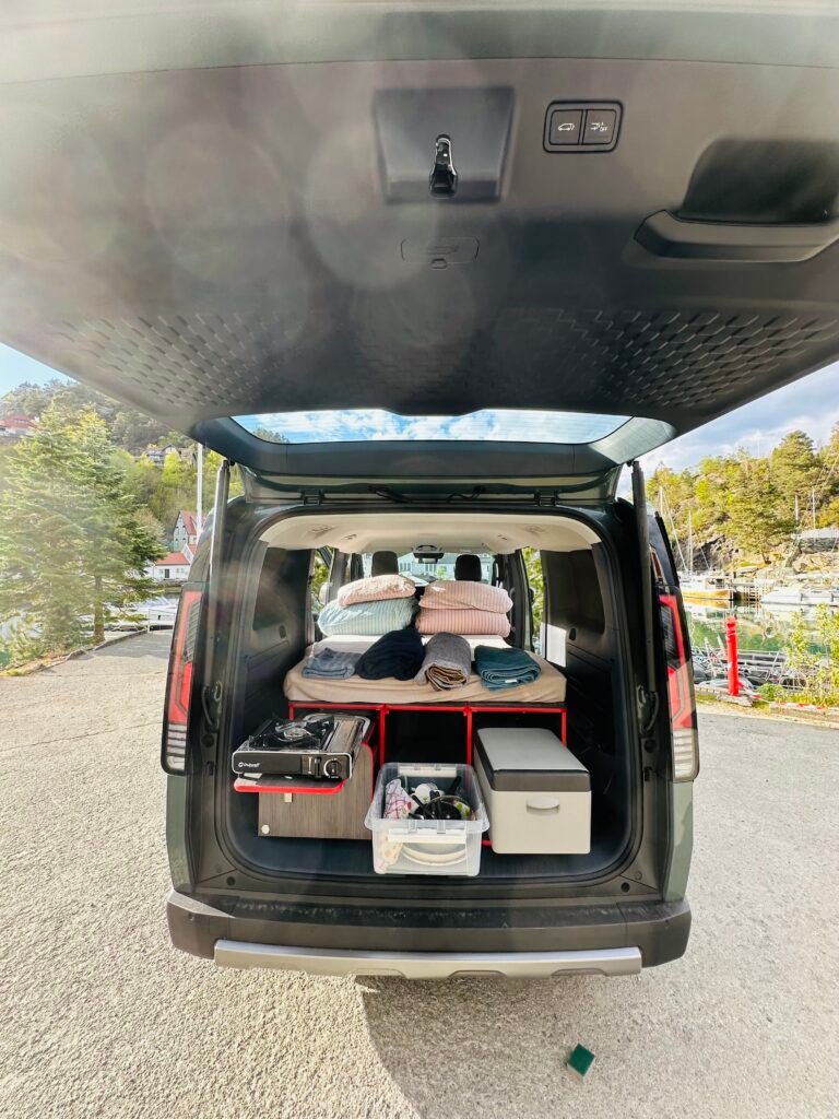 Rear of a SUV with trunk open, packed with folded blankets, towels, cooler, storage bins and camping gear ready for a trip.