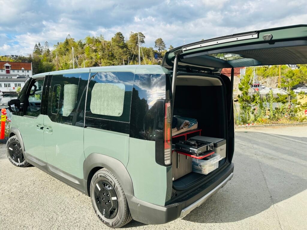Green van with rear cargo door open, showing a small organized storage area and shelving inside by the tailgate.